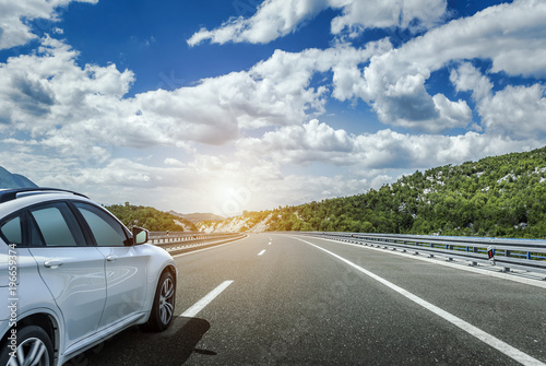 A white car rushing along a high-speed highway in the sun.