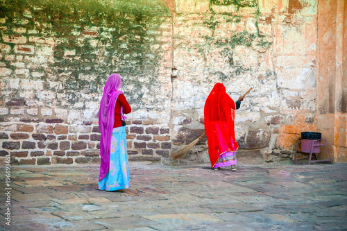 Two indian women are cleaning the stone antique street with broom in India