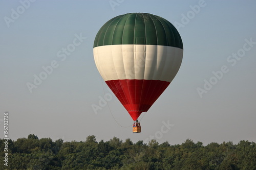 Balon na rozgrzane powietrze, w pasy zielony, biały i czerwony, w powietrzu, ponad drzewami