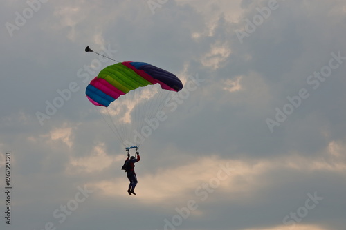 Paralotniarz ląduje, kolorowa czasza spadochronu, w tle pochmurne niebo