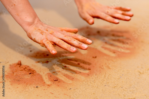 Woman hands creating shapes with red sand on the beach in aboriginal art style