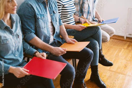 Close up view of young people sitting in chairs with folders before the job interview in the waiting room.