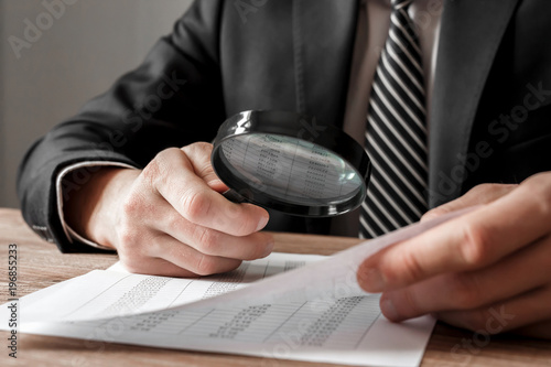 Businessman holding magnifying glass zoom and analyzing financial indicators