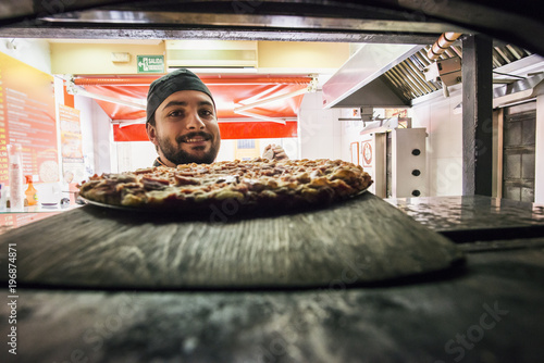 inside view of man cooking a pizza in owen at store