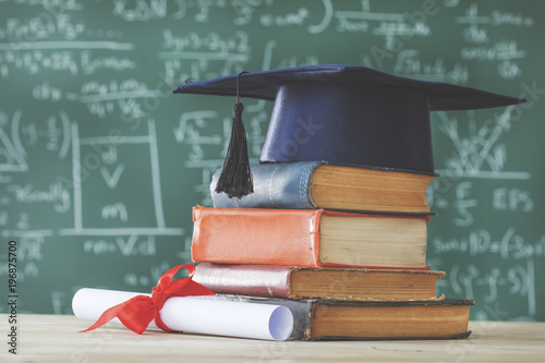 Stack books graduate hat and diploma in front of green chalkboard