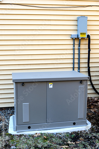 Residential generator on concrete pad, next to a house wall
