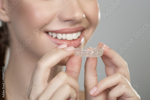 Straight teeth. Close up of hands of joyful girl with aligner for orthodontic correction. Oral care concept. Isolated background