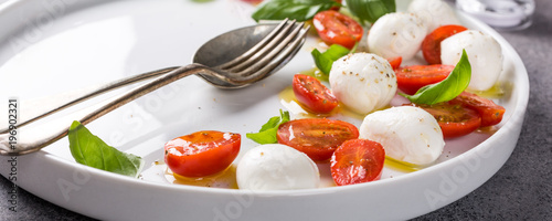 Delicious caprese salad with ripe cherry tomatoes and mini mozzarella cheese balls with fresh basil leaves. Italian healthy food concept with copy space. Banner.