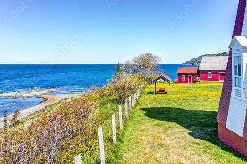 Red painted shed with yellow dandelion flowers and view of Saint Lawrence river in La Martre in the Gaspe Peninsula, Quebec, Canada, Gaspesie region farm