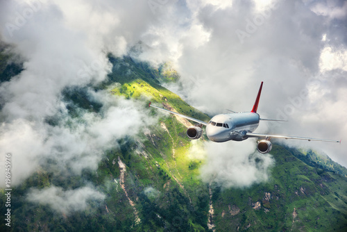 Aerial view of aircraft. Airplane is flying in clouds over mountains with forest at sunset. Landscape with passenger airplane, cloudy sky, trees. Passenger aircraft. Business travel. Commercial plane