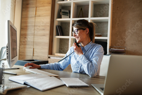 Businesswoman in her office.She sitting at the desk and talking on the phone.