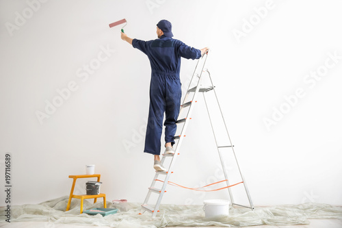 Young male decorator painting wall in empty room