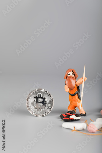 Ancient man from modelling clay and bitcoin on gray surface.