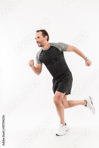 Photo in profile of content energetic sportsman 30s wearing shorts and t-shirt smiling and running marathon or doing workout, isolated over white background