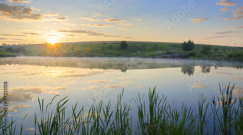 . Sunny summer morning.Foggy landscape with river.Beautiful clouds in sky.Fog over the water.Warm sunlight at sunrise.River Krasivaya in Tula region,Russia. 