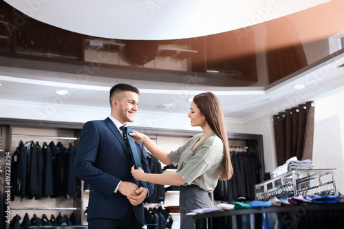 Female shop assistant helping man to choose suit in store