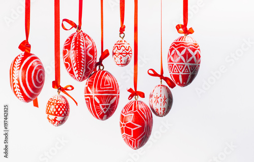 Red easter eggs with folk Ukrainian pattern hang on red ribbons from left side on white background. Ukrainian traditional eggs pisanka and krashanka.