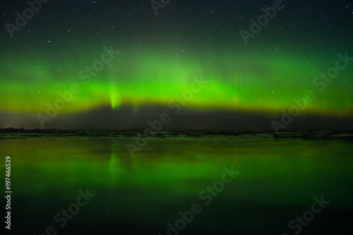 Night sky view of beautiful green aurora borealis (northern polar lights) in Finland with reflection on the frozen and snowy lake during geomagnetic storm at expedition