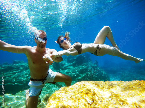 Underwater photo of young satisfied joyful love couple exploring and enjoying with goggles in the exotic turquoise sea near the coral reef while holding hands together.