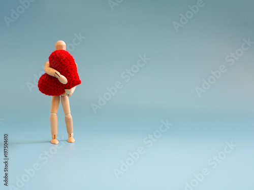 Wooden puppet standing and holding a red heart on the blue screen background. Wooden puppet holding the heart with love and care. Concept of take care and love.