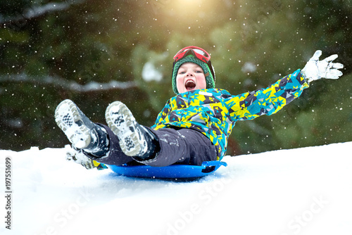  Boy sledding in a snowy forest. Outdoor winter fun for Christmas vacation.