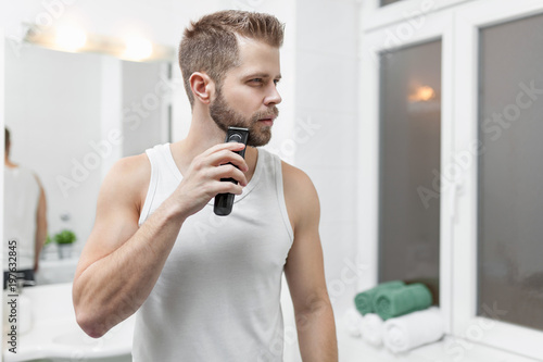 Handsome bearded man trimming his beard with a trimmer