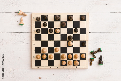 Top view on wooden chess board with figures during the game on white wooden table background