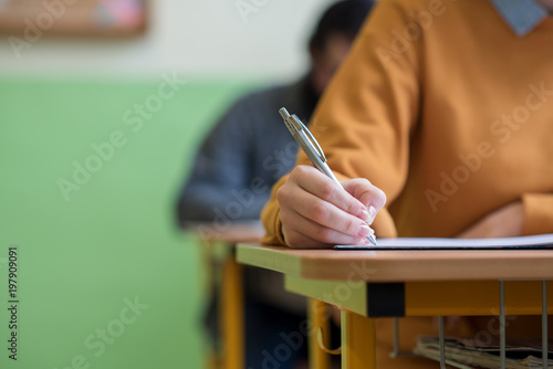 Students taking exam in classroom. Education test and literacy concept. Cropped shot, hand detail.