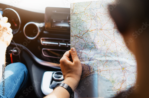 Hipster man holding in male hands and looking on navigation map in auto, tourist traveler hiker driving on background view way road, trip in transportation, person sitting on backdrop window auto