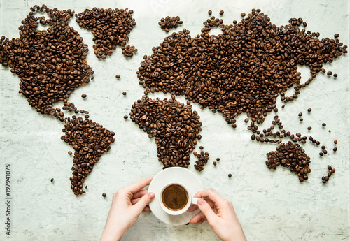 Hands hold a cup of coffee against the background of the world map from coffee beans
