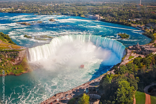 Aerial top landscape view of Niagara Falls and tour boat in water between US and Canada. Horseshoe of famous Canadian waterfall on sunny day
