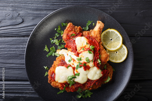 La milanesa napolitana - homemade veal cutlet with mozzarella cheese, lemon and tomato sauce close-up. horizontal top view