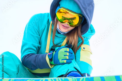 Young snowboarder holding her injured leg.