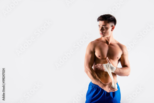 I'm in tune of winning. Portrait of sportive muscular naked, wearing blue shorts bodybuilder, he is using bandage to cover hands, preparation to competition isolated on white background, copy-space