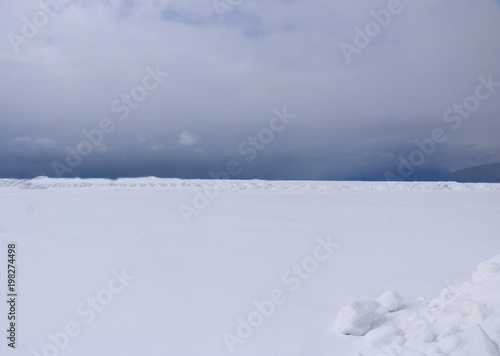 snow field. The plain is covered with white snow under a blue sky with thick white clouds. before a snowfall, a storm, a snowstorm. premonition of a blizzard. in anticipation of a blizzard.
