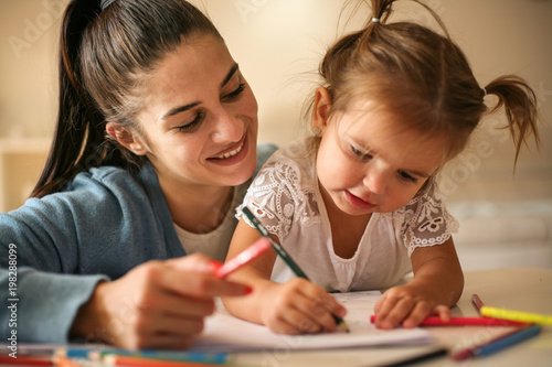 Mother helping her little girl to writing.