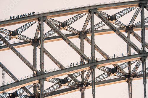 Tourists climb on two layers of the Sydney Harbour Bridge. The sun is catching the bottom of the metal bridge.