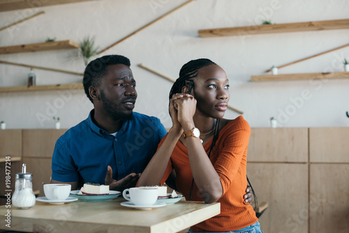 insulted african american woman with boyfriend sitting at table in cafe