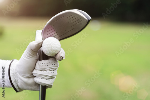 Golf background concept. Closeup golf ball and golf club on hand with glove with blurred green grass on background. Picture for add text message. Backdrop for design art work.
