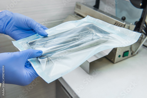 Close up dentist assistant's hands holding packaged with vacuum packing machine medical instruments ready for sterilizing in autoclave. Dental office. Selective focus, space for text.