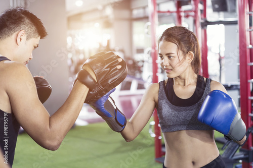 Mężczyzna trener trzymając rękawice sportowe w siłowni i kobiece rękawice. Kobieta treningu boksu w sali fitness klasy. Ćwiczenia boksu sportowego.