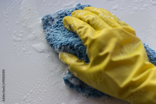 A female hand in a yellow glove washes a soapy rag surface. White background, isolated