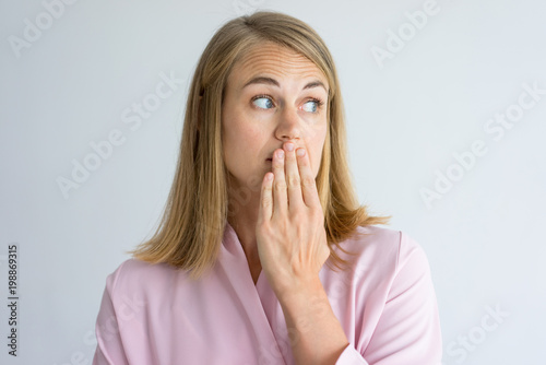 Portrait of shocked young Caucasian woman wearing pink blouse covering mouth with hand. Fear, bad breath concept