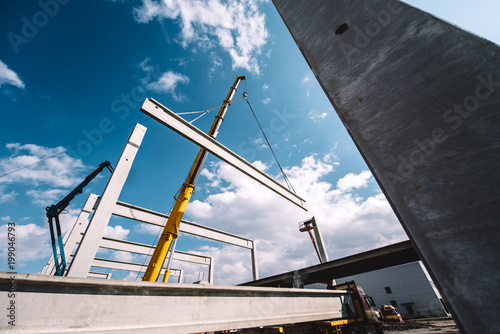 Construction site of prefabricated hall with cement pillars and concrete beams moving crane