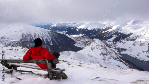 backcountry skier takes a break and sit on a summit bench and enjoys the view of Davos in winter