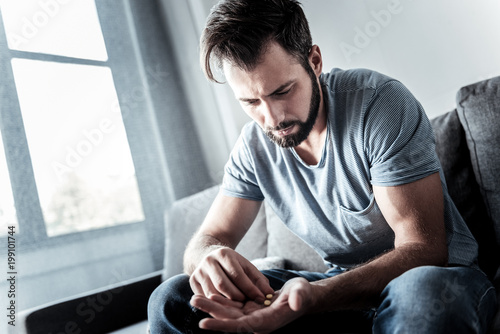 My daily dose. Sad depressed moody man sitting on the sofa and looking at the pills while being ready to take them