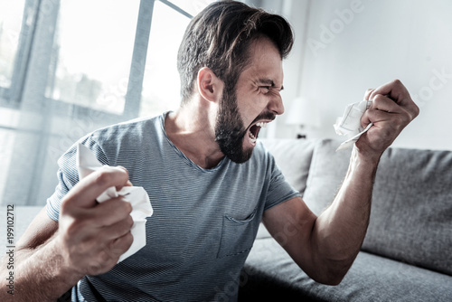 Nervous breakdown. Angry unhappy emotional man holding crumpled paper and crying while expressing his emotions