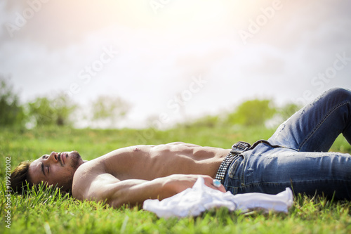Good looking, shirtless fit male model relaxing lying on the grass, shot from above
