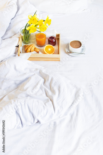 Morning breakfast in bed wooden tray with a cup of coffee croissant orange juice fresh orange jam bouquet of flowers daffodils. Top view Morning at Hotel Background Concept Interior Copy Space