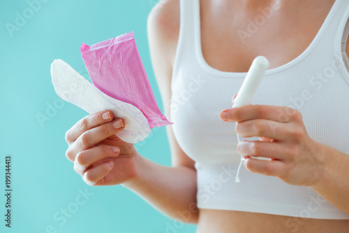 Young woman with a menstrual compress and a tampon on blue background.